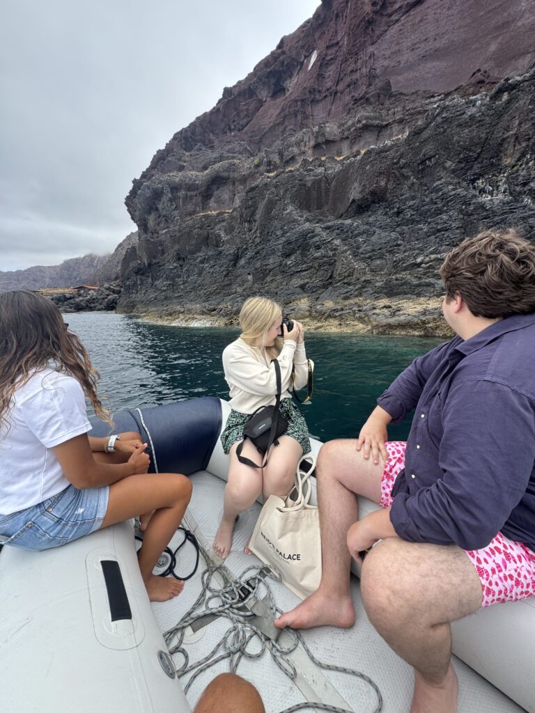 Three friends on an Luxury Yacht Charter to Desertas photograph towering red volcanic cliffs over calm waters under overcast skies, an experience by Luxury Charter Madeira.