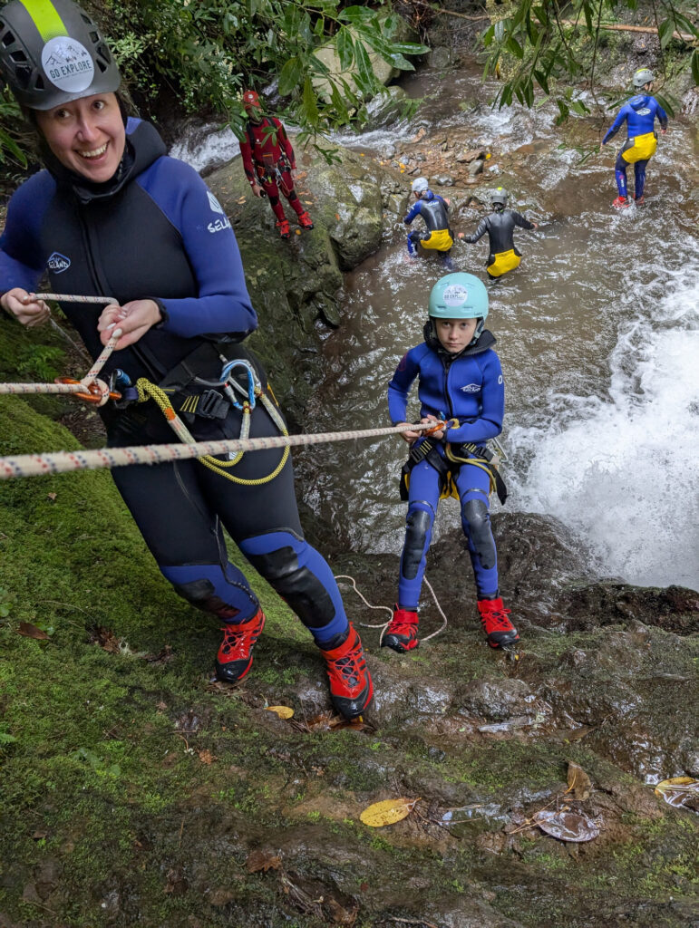 Best canyoning experiences in Madeira 1 A female canyoneer helps a young child rappeller while the group watches in Porto Novo, Camacha, during a Beginner Level 1 canyoning tour with Go Explore Madeira.