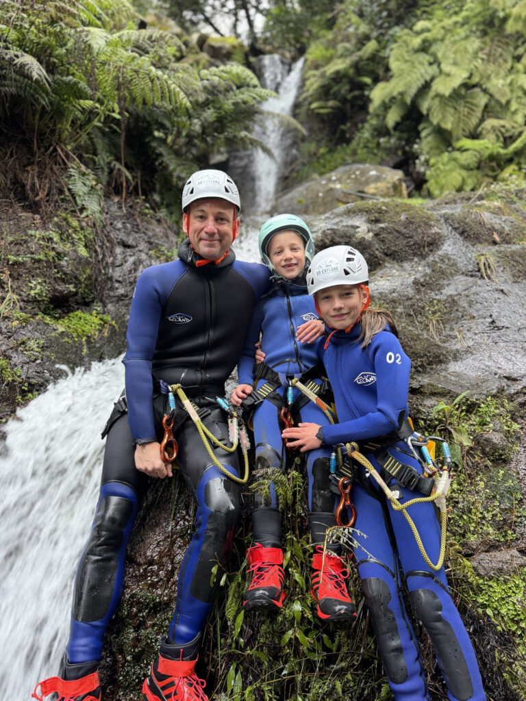 Best canyoning experiences in Madeira 4 A father sits with his two children on rocks beside a fern-lined waterfall in Porto Novo, Camacha, during a Beginner Level 1 canyoning tour with Go Explore Madeira.