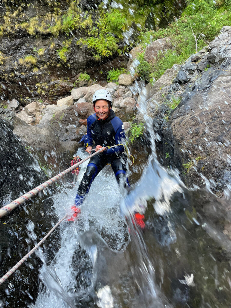 A smiling canyoneer rappels down a mossy waterfall in Ribeira do Cidrão, Nuns Valley, amid an Intermediate Level 2 canyoning tour with Go Explore Madeira.