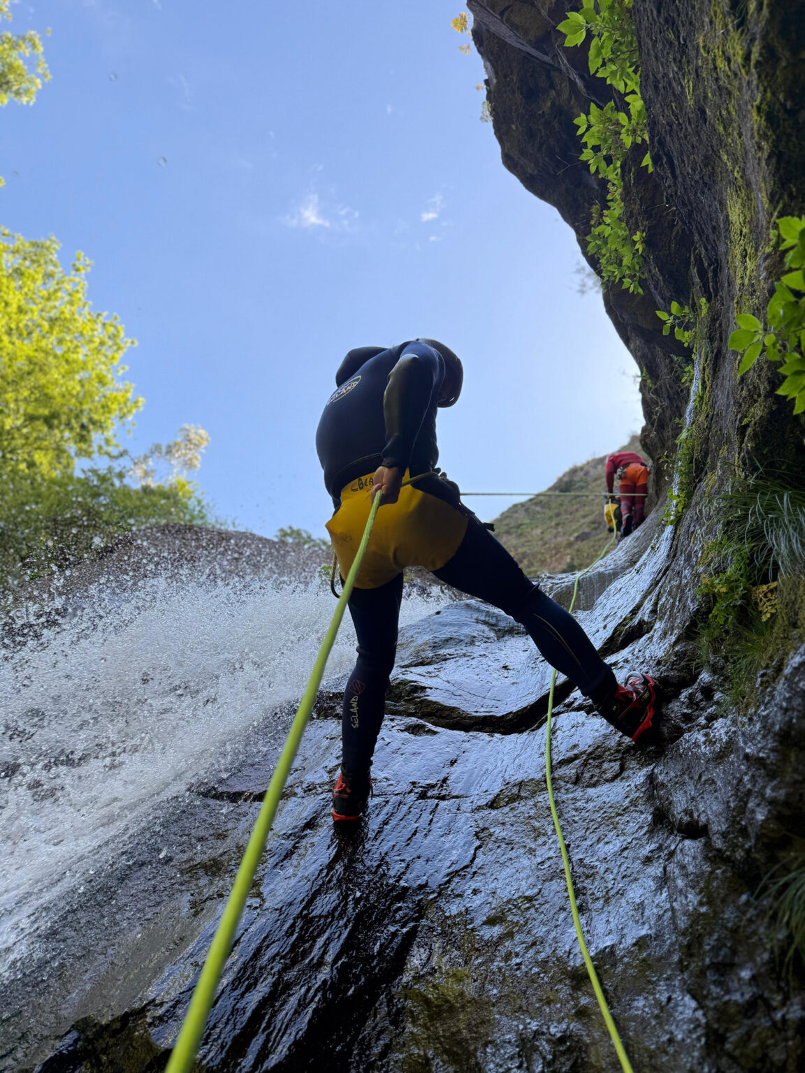 Two canyoneers abseil a sunny rock slide waterfall in Ribeira do Cidrão, Nuns Valley, as part of an Intermediate Level 2 canyoning tour with Go Explore Madeira.