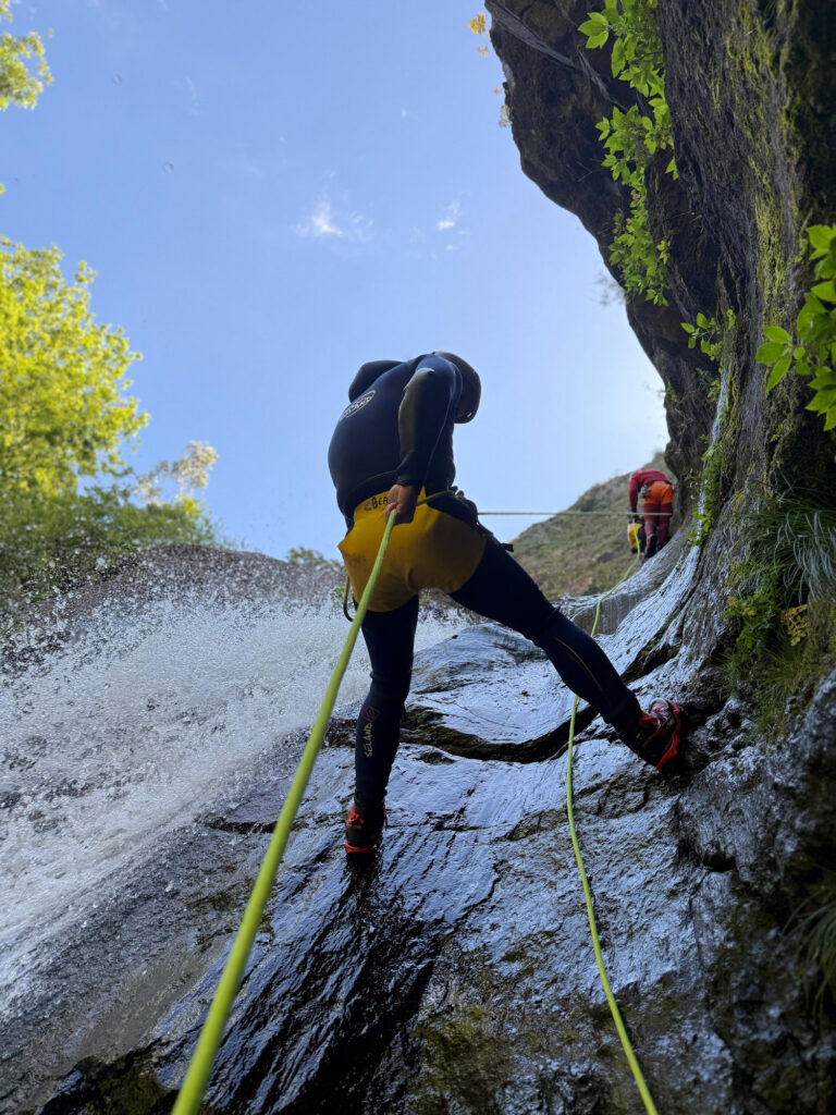 Two canyoneers abseil a sunny rock slide waterfall in Ribeira do Cidrão, Nuns Valley, as part of an Intermediate Level 2 canyoning tour with Go Explore Madeira.
