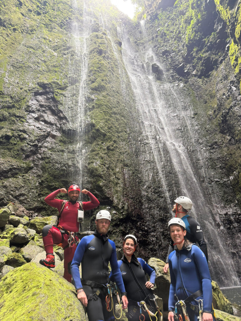 Best canyoning experiences in Madeira 6 A group of canyoneers poses at the base of a towering waterfall in Ribeira Funda Inferior after an Advanced Level 3 canyoning descent with Go Explore Madeira.