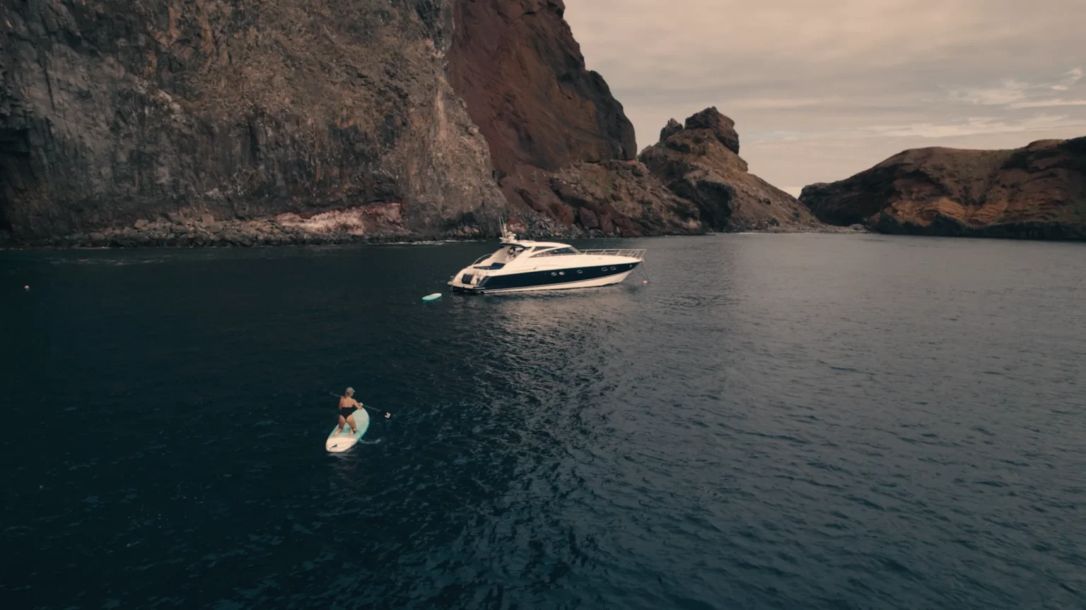 Luxury Madeira Yacht Charter Rental in the sea near the coast of Madeira and a woman on top of a paddle board rowing, an experience by Luxury Charter Madeira.