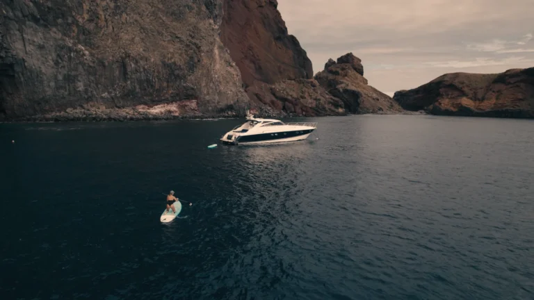 Luxury Madeira Yacht Charter Rental in the sea near the coast of Madeira and a woman on top of a paddle board rowing, an experience by Luxury Charter Madeira.