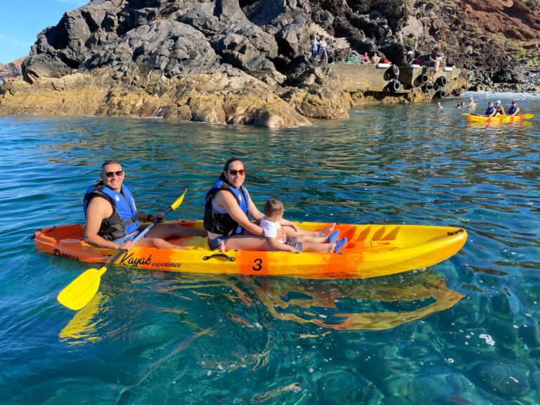 Two orange kayaks paddle alongalong Cais do Sardinha coastline, with life-vested explorers enjoying the turquoise waters and sunny skies, a Kayaking experience by Madeira Sea Emotions.