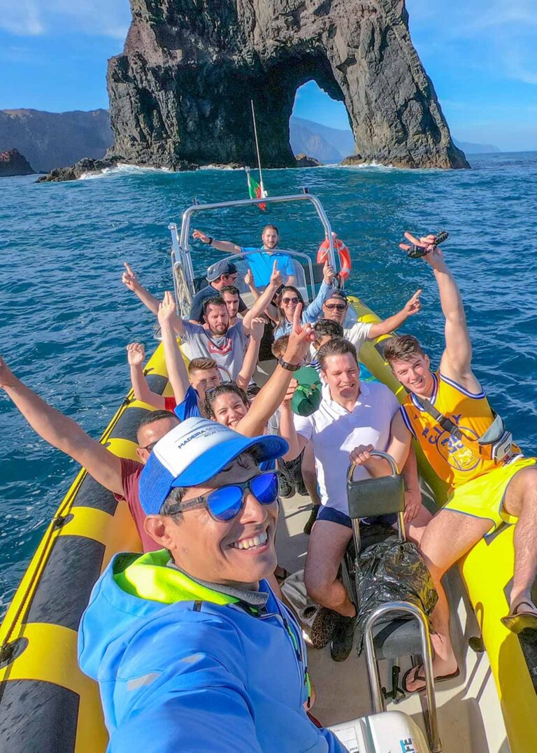 Group enjoying our 4h Day Pack fun in a boat tour at Ponta de São Lourenço, celebrating on a yellow speedboat in front of the iconic sea arch during a boat tour experience by Madeira Sea Emotions.