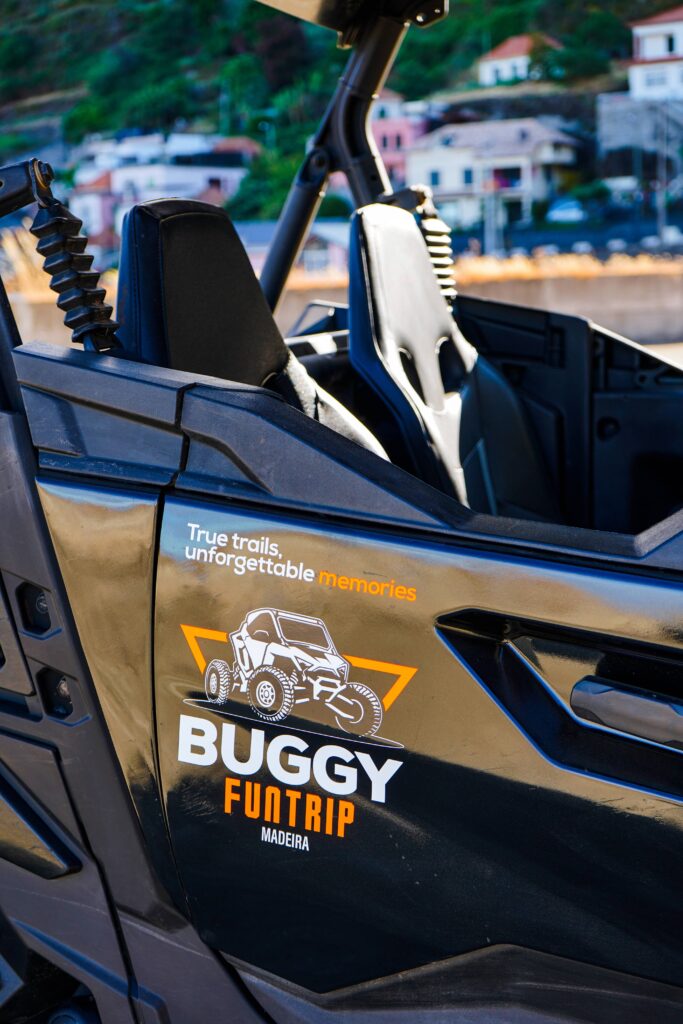 Side view of a Buggy Funtrip off-road buggy in Madeira Island, showing the open seats and branded door decal with the slogan “True trails, unforgettable memories.” from Buggy Funtrip Madeira company.
