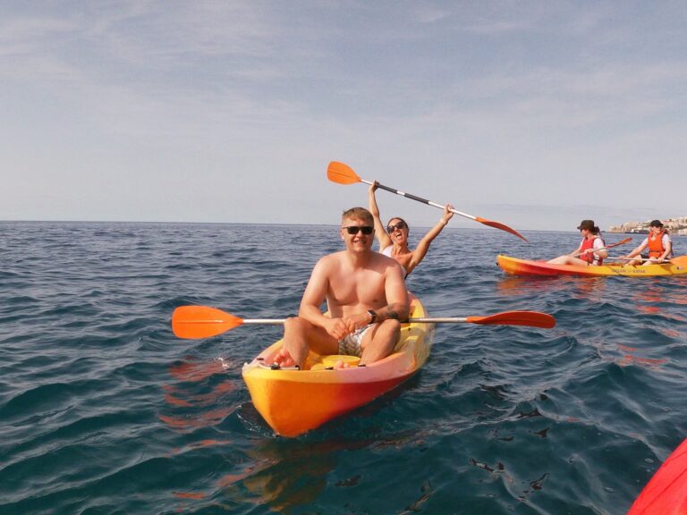 Couple kayaking on the ocean during a Madeira Radical Kayak Funchal Tour, an experience by Madeira Radical, with other participants paddling nearby on the calm blue water.