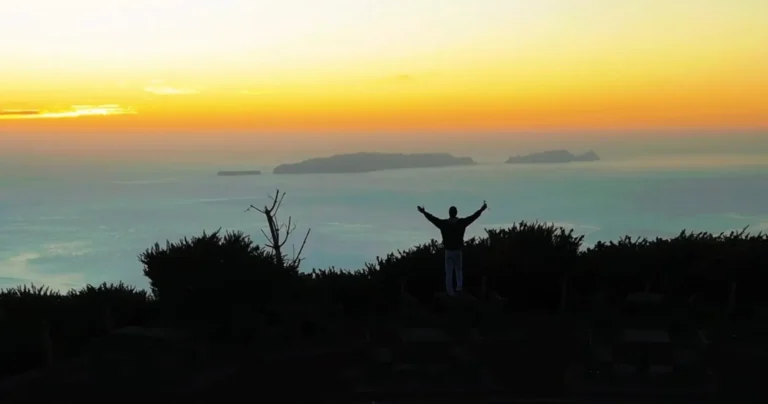 A man spreading his arms while contemplating the sunset over the sea, a view from the east coast of Madeira, an experience by Sea La Vie Mountain Expedition.