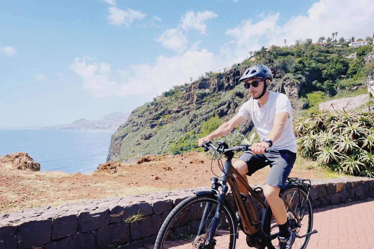 Rider on an e-bike enjoying a sunny cliffside viewpoint over the Atlantic Ocean on the Self-Guided E-Bike Road Tour From Funchal to Garajau, an experience by MADcycle.