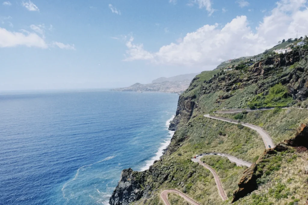Dramatic cliffside viewpoint over the Atlantic Ocean and winding coastal road on the Self-Guided E-Bike Road Tour From Funchal to Garajau, an experience by MADcycle.