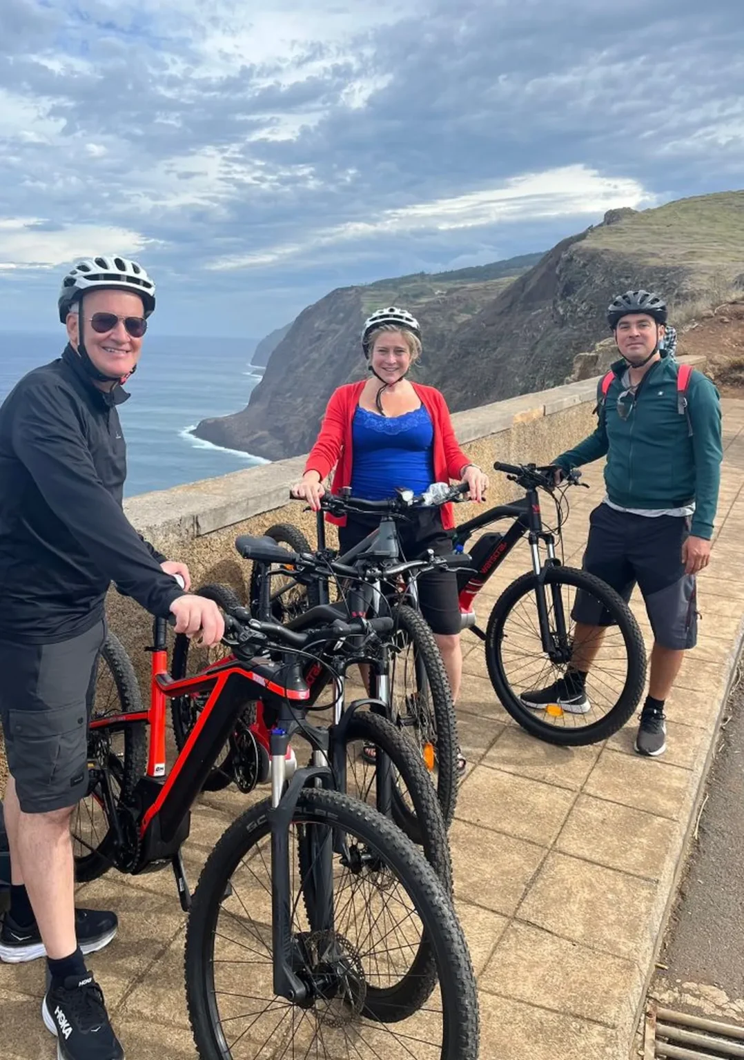 Three riders posing with their e-bikes at a dramatic cliffside viewpoint above the ocean on the Bike tour on the west coast of Madeira, an experience by Madeira Island Route.