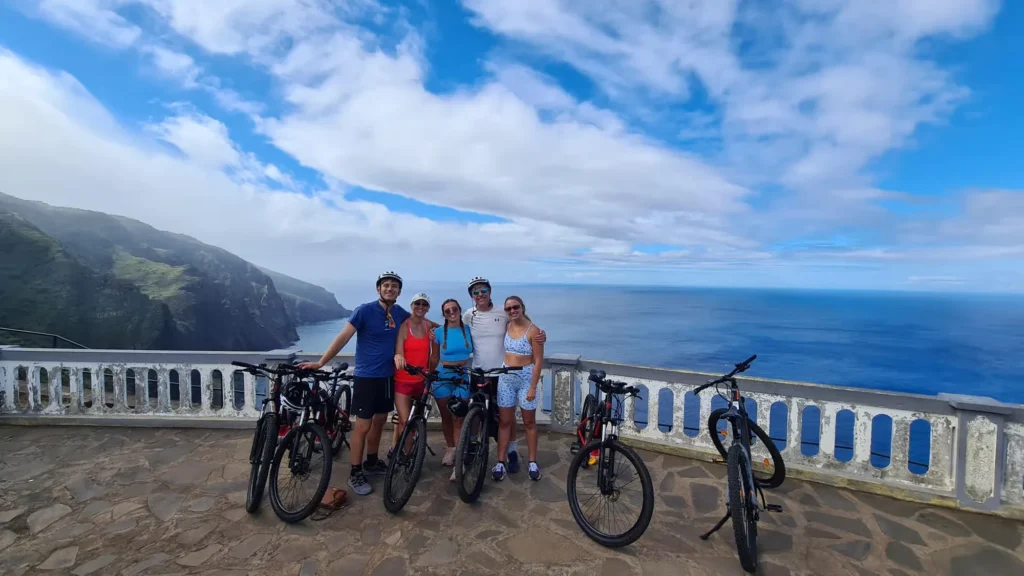 Group of riders with e-bikes posing at a scenic ocean viewpoint on the Bike tour on the west coast of Madeira, an experience by Madeira Island Route.