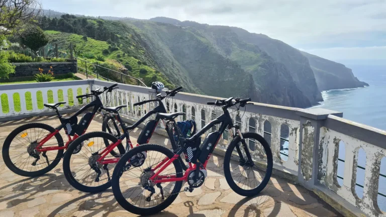 Row of e-bikes parked at a cliffside viewpoint overlooking the dramatic green coastline on the Bike tour on the west coast of Madeira, an experience by Madeira Island Route.