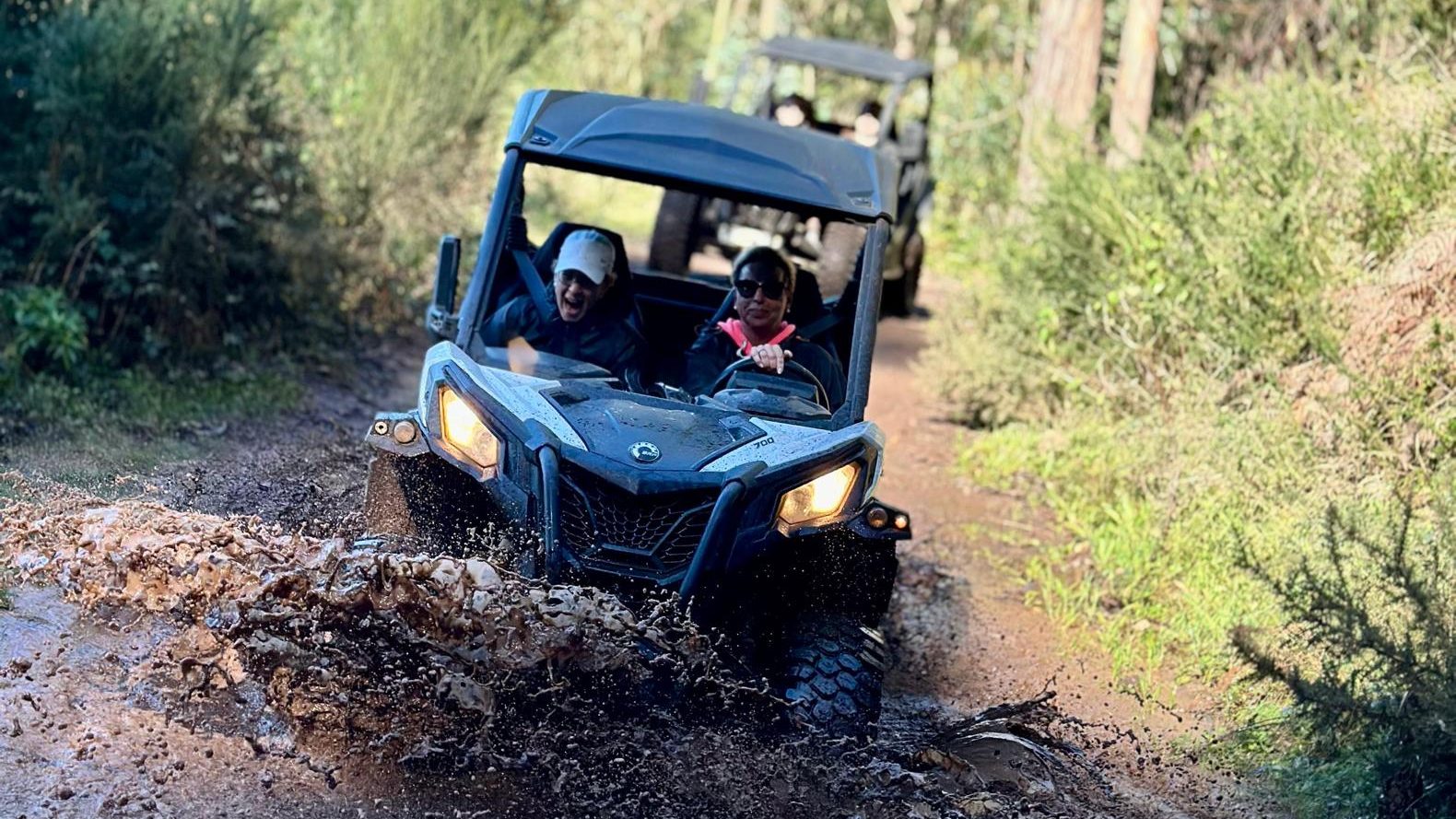Which Buggy Tour in Madeira Is Right for You 1 Buggy splashing through a muddy puddle on a forest trail near Câmara de Lobos, with another vehicle following behind among the green trees, during an adventure buggy tour by Madeira Radical.