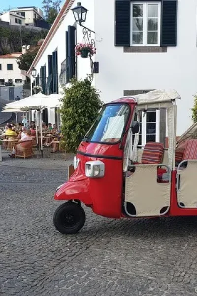 Red tuk tuk parked on the cobbled square in Câmara de Lobos, with café terraces and the village behind