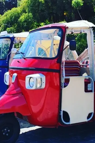 Red, blue and white tuk tuks parked in a row on a cobbled street in Funchal