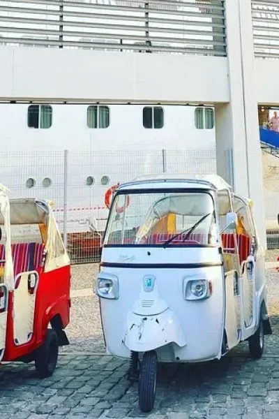 Red, white and blue tuk tuks parked on the quay in front of a docked cruise ship at Funchal port