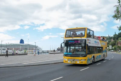 An Hop-on Hop-off Bus near Funchal marina with a cruise ship on the back, an experience by Carristur.