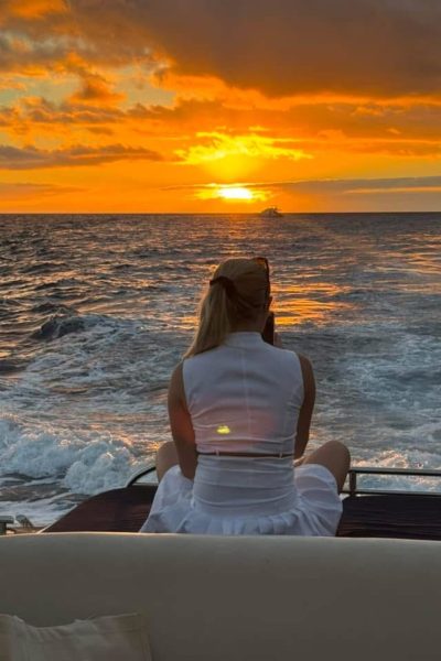 A woman seated recording with her phone the sunset on the sea and the coast of Madeira in a deck of a Luxury Madeira Yacht Charter Rental by Luxury Charter Madeira.