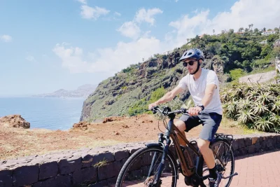Rider on an e-bike enjoying a sunny cliffside viewpoint over the Atlantic Ocean on the Self-Guided E-Bike Road Tour From Funchal to Garajau, an experience by MADcycle.