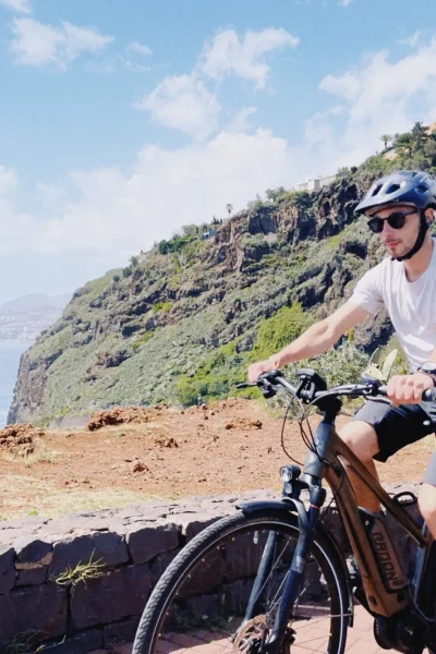 Rider on an e-bike enjoying a sunny cliffside viewpoint over the Atlantic Ocean on the Self-Guided E-Bike Road Tour From Funchal to Garajau, an experience by MADcycle.