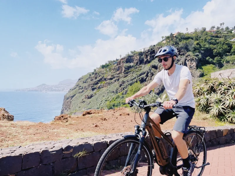 Rider on an e-bike enjoying a sunny cliffside viewpoint over the Atlantic Ocean on the Self-Guided E-Bike Road Tour From Funchal to Garajau, an experience by MADcycle.
