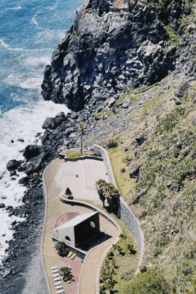 Aerial view of a modern seaside terrace and winding cliffside path above the Atlantic Ocean on the Self-Guided E-Bike Road Tour From Funchal to Garajau, an experience by MADcycle.