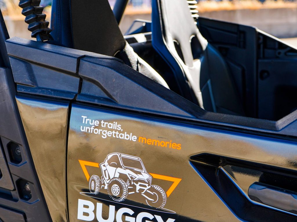 Side view of a Buggy Funtrip off-road buggy in Madeira Island, showing the open seats and branded door decal with the slogan “True trails, unforgettable memories.” from Buggy Funtrip Madeira company.