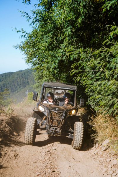 Buggy driving up a dusty mountain trail beside dense green vegetation during an off-road adventure in Madeira, during an adventure buggy tour by Buggy Funtrip Madeira