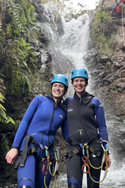 Two smiling female friends embrace in wetsuits by a waterfall in Porto Novo, Camacha, during a Beginner Level 1 canyoning tour with Go Explore Madeira.