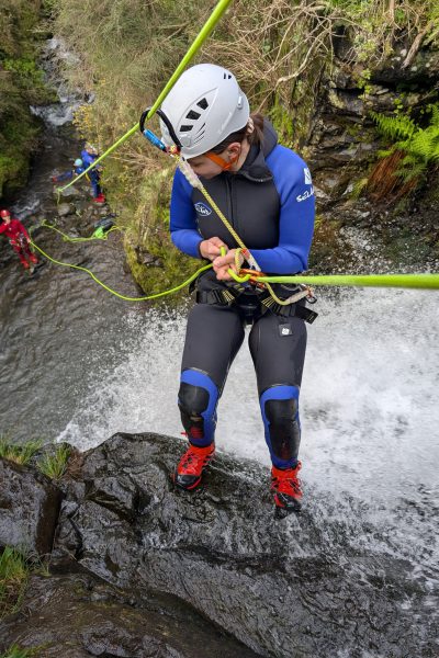 A female canyoneer prepares her ropes at the edge of a small waterfall in Porto Novo, Camacha, with group members visible below during a Beginner Level 1 tour with Go Explore Madeira.