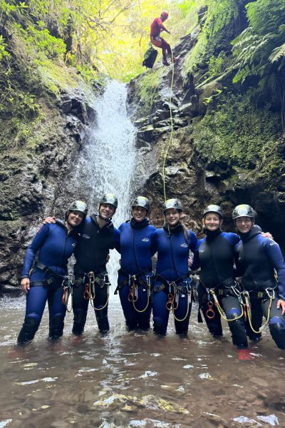 A group of canyoneers cheers in shallow waters as their instructor abseils a waterfall in Porto Novo, Camacha, during a Begginner Level 1 canyoning tour with Go Explore Madeira.