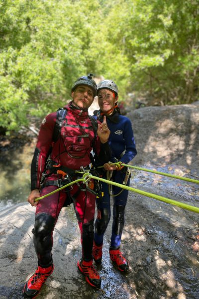 Two canyoneers stand secured on a rocky ledge in Ribeira do Cidrão, Nuns Valley, preparing their ropes for an Intermediate Level 2 canyoning experience with Go Explore Madeira.