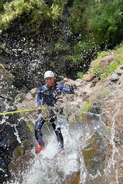 A joyful canyoneer wades through splashing waters at the base of a waterfall in Ribeira do Cidrão, Nuns Valley, during an Intermediate Level 2 canyoning experience with Go Explore Madeira.