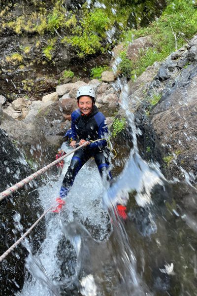 A smiling canyoneer rappels down a mossy waterfall in Ribeira do Cidrão, Nuns Valley, amid an Intermediate Level 2 canyoning tour with Go Explore Madeira.