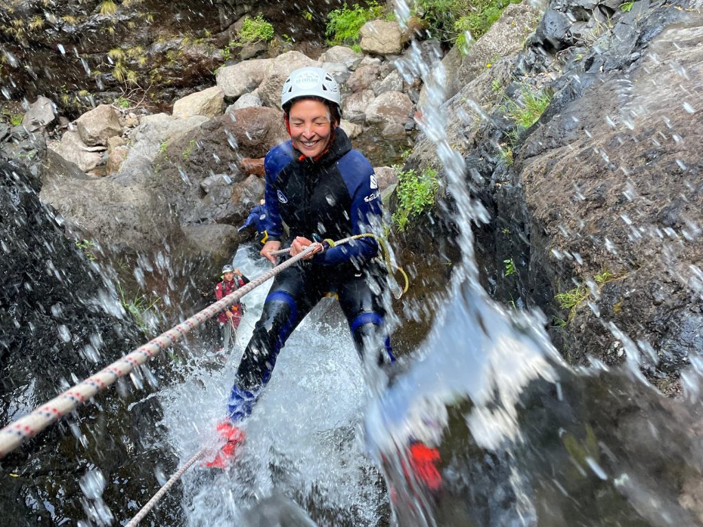 A smiling canyoneer rappels down a mossy waterfall in Ribeira do Cidrão, Nuns Valley, amid an Intermediate Level 2 canyoning tour with Go Explore Madeira.