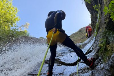 Two canyoneers abseil a sunny rock slide waterfall in Ribeira do Cidrão, Nuns Valley, as part of an Intermediate Level 2 canyoning tour with Go Explore Madeira.