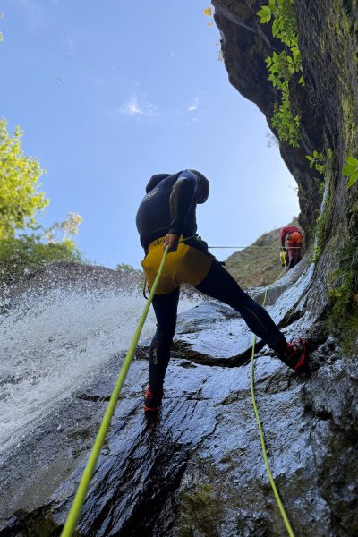 Two canyoneers abseil a sunny rock slide waterfall in Ribeira do Cidrão, Nuns Valley, as part of an Intermediate Level 2 canyoning tour with Go Explore Madeira.