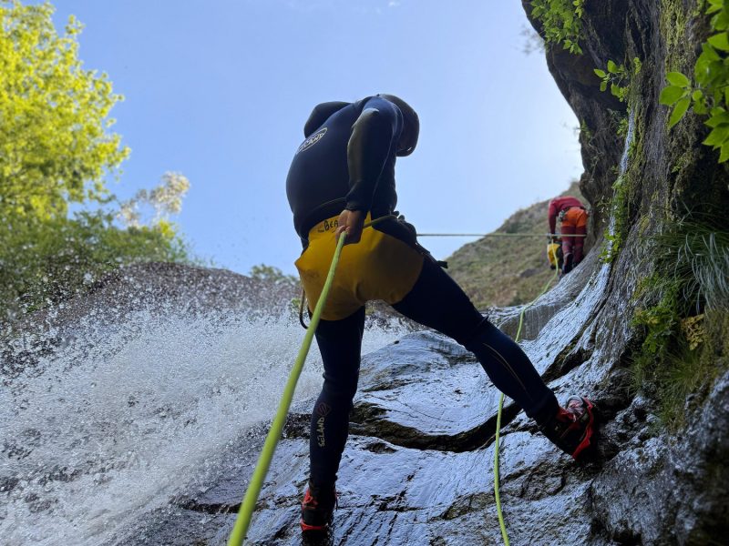 Two canyoneers abseil a sunny rock slide waterfall in Ribeira do Cidrão, Nuns Valley, as part of an Intermediate Level 2 canyoning tour with Go Explore Madeira.