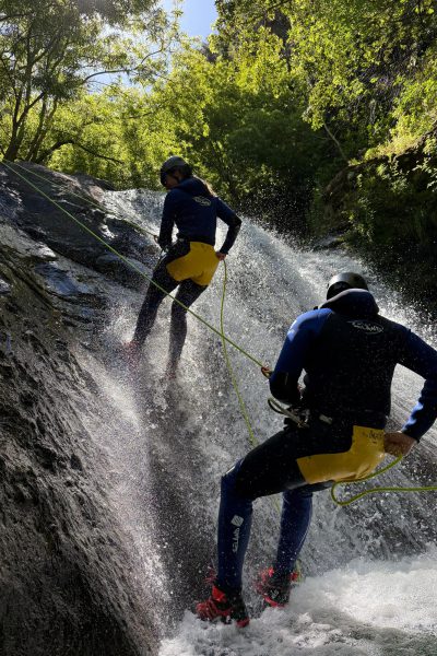 Two canyoneers abseil down a sunlit waterfall slide in Ribeira do Cidrão, Nuns Valley, during an Intermediate Level 2 canyoning adventure with Go Explore Madeira.