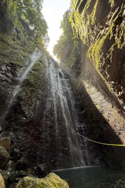 Canyoneer abseils a towering sunlit waterfall in Ribeira Funda Inferior during an Advanced Level 3 canyoning experience with Go Explore Madeira.