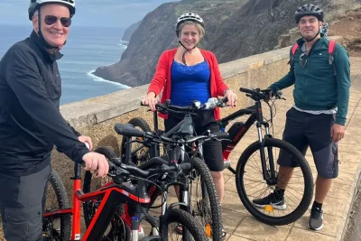 Three riders posing with their e-bikes at a dramatic cliffside viewpoint above the ocean on the Bike tour on the west coast of Madeira, an experience by Madeira Island Route.