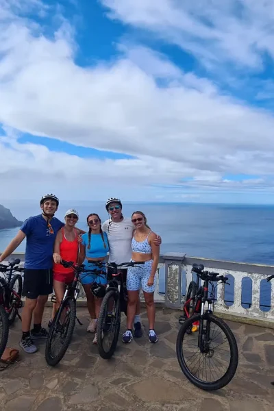 Group of riders with e-bikes posing at a scenic ocean viewpoint on the Bike tour on the west coast of Madeira, an experience by Madeira Island Route.