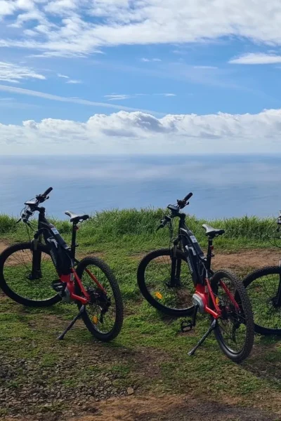 Row of e-bikes parked on a grassy cliff edge overlooking the Atlantic Ocean on the Bike tour on the west coast of Madeira, an experience by Madeira Island Route.