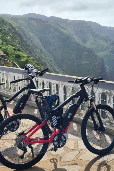 Row of e-bikes parked at a cliffside viewpoint overlooking the dramatic green coastline on the Bike tour on the west coast of Madeira, an experience by Madeira Island Route.