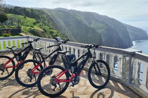 Row of e-bikes parked at a cliffside viewpoint overlooking the dramatic green coastline on the Bike tour on the west coast of Madeira, an experience by Madeira Island Route.
