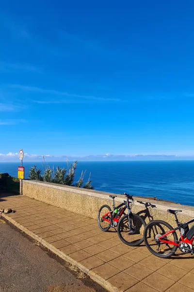 E-bikes parked beside the Ponta do Pargo lighthouse overlooking the Atlantic Ocean under a clear blue sky on the Bike tour on the west coast of Madeira, an experience by Madeira Island Route.