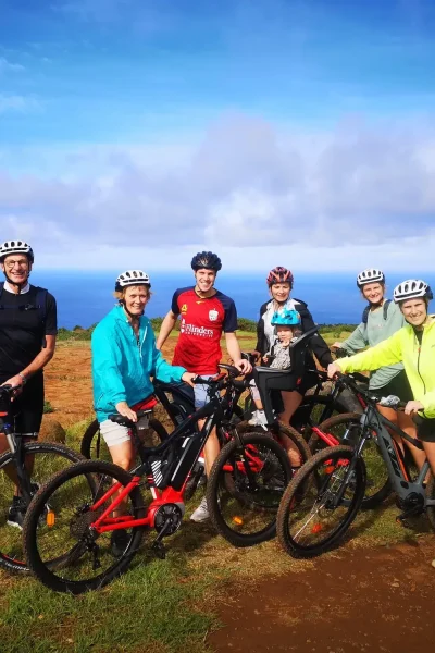 Group of riders with e-bikes posing on a grassy clifftop with wide ocean views on the Bike tour on the west coast of Madeira, an experience by Madeira Island Route.